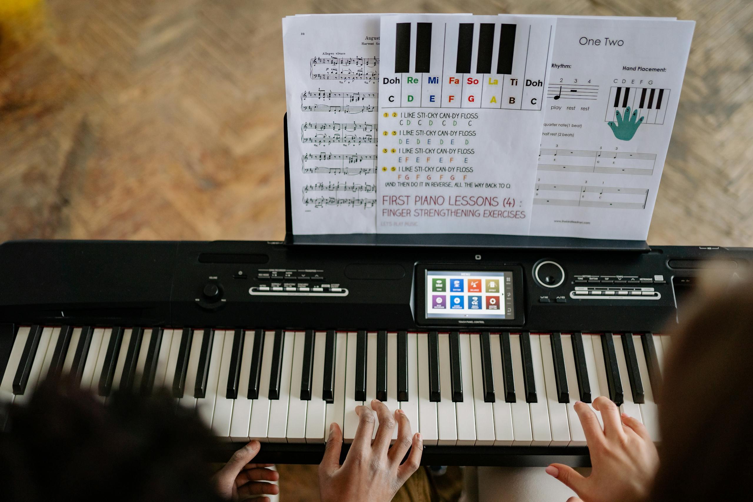 Adults learning piano with music sheets, viewed from above.